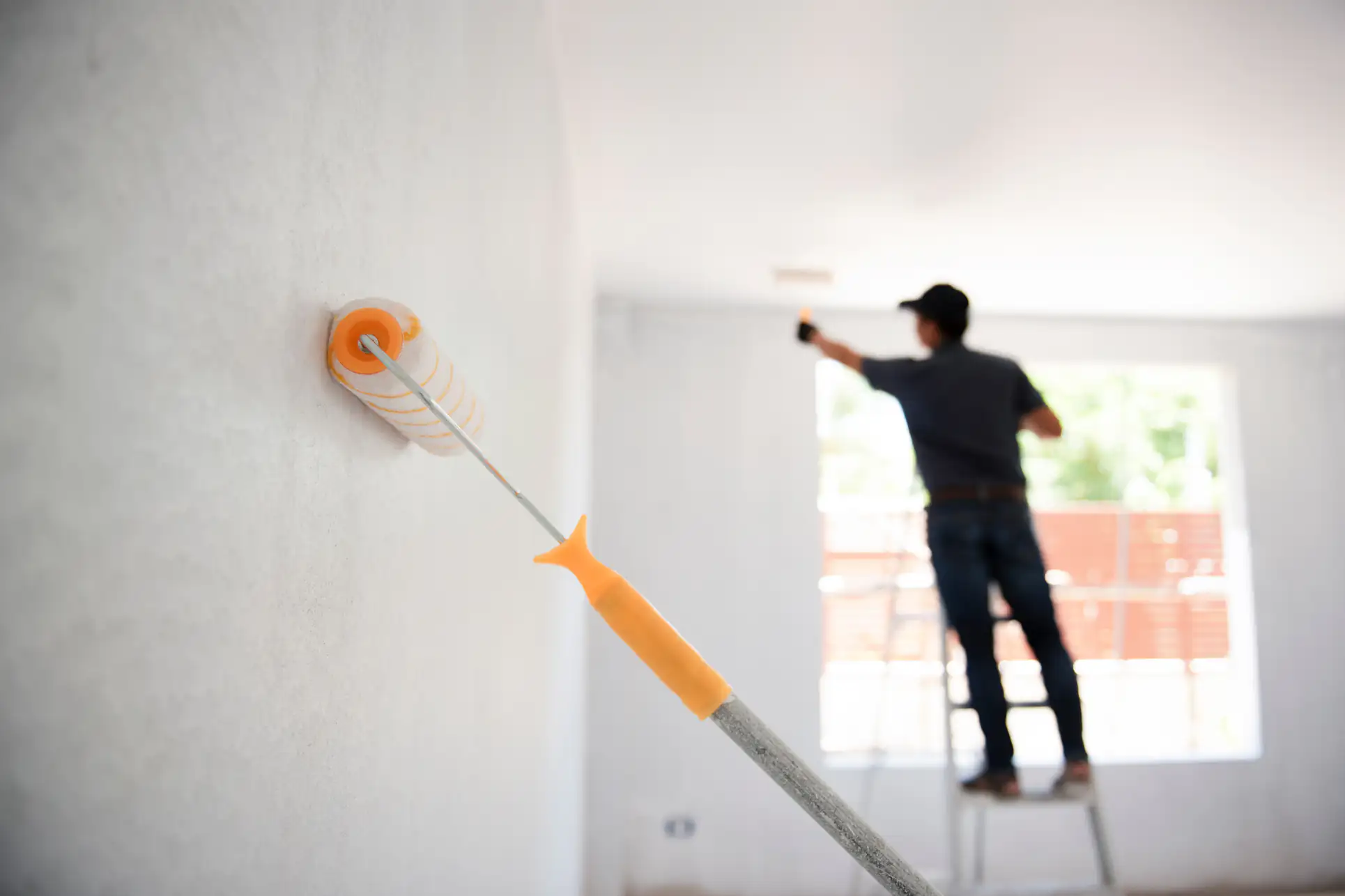 A professional painter using a roller to apply a fresh coat of paint in a bright, well-lit room in Essex County, Massachusetts, showcasing Fine Coat Painters' expert interior services